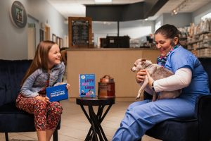 A fifth-grader interviewer laughing with a Vet Tech holding an old chihuahua.
