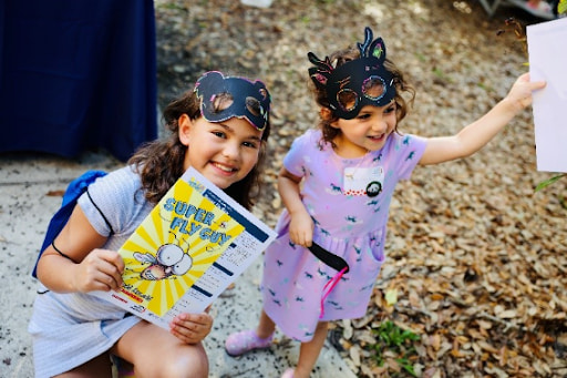 Two girls smiling and holding books while wearing animal masks.
