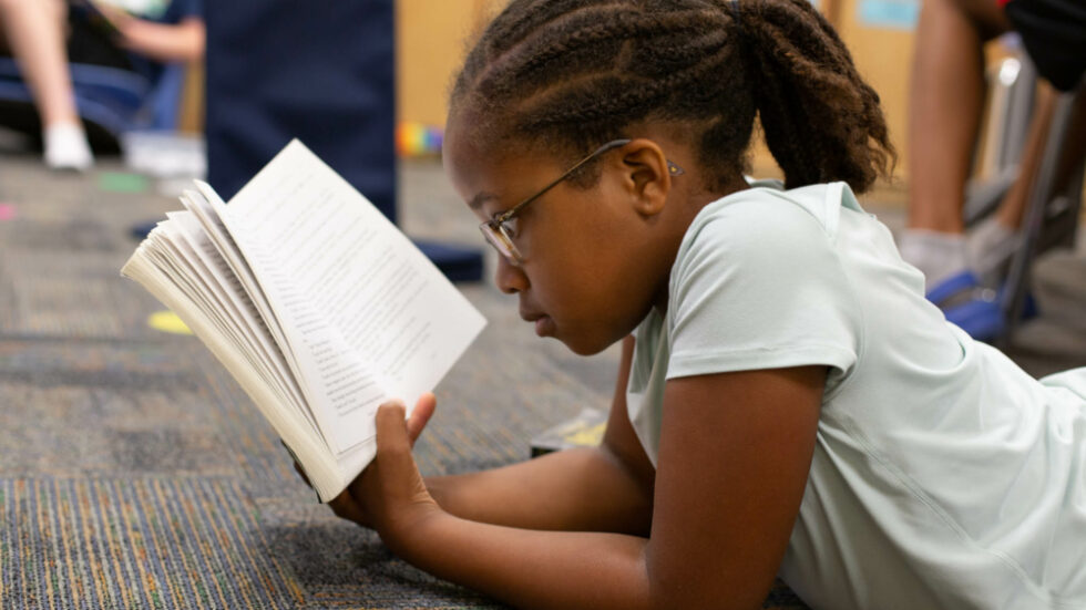 A young student reading a book while laying on the floor at the school PK Yonge.