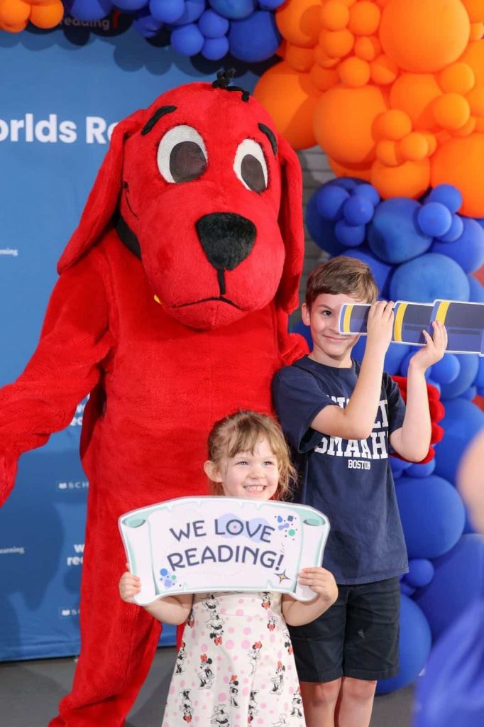A person costumed as Clifford the Big Red Dog taking photos with two siblings at the 2025 Book Bash in Tampa, Florida.