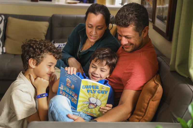 A family gathers on the couch to read the children's book Super Fly Guy. 