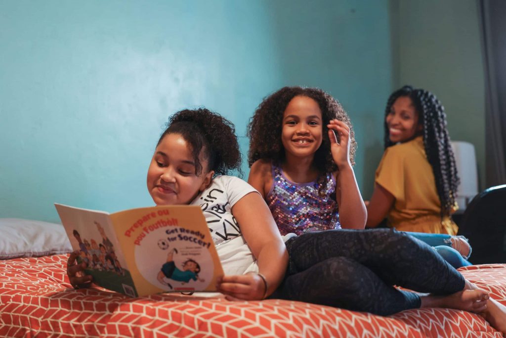 Two girls reading a book about soccer on their bed.