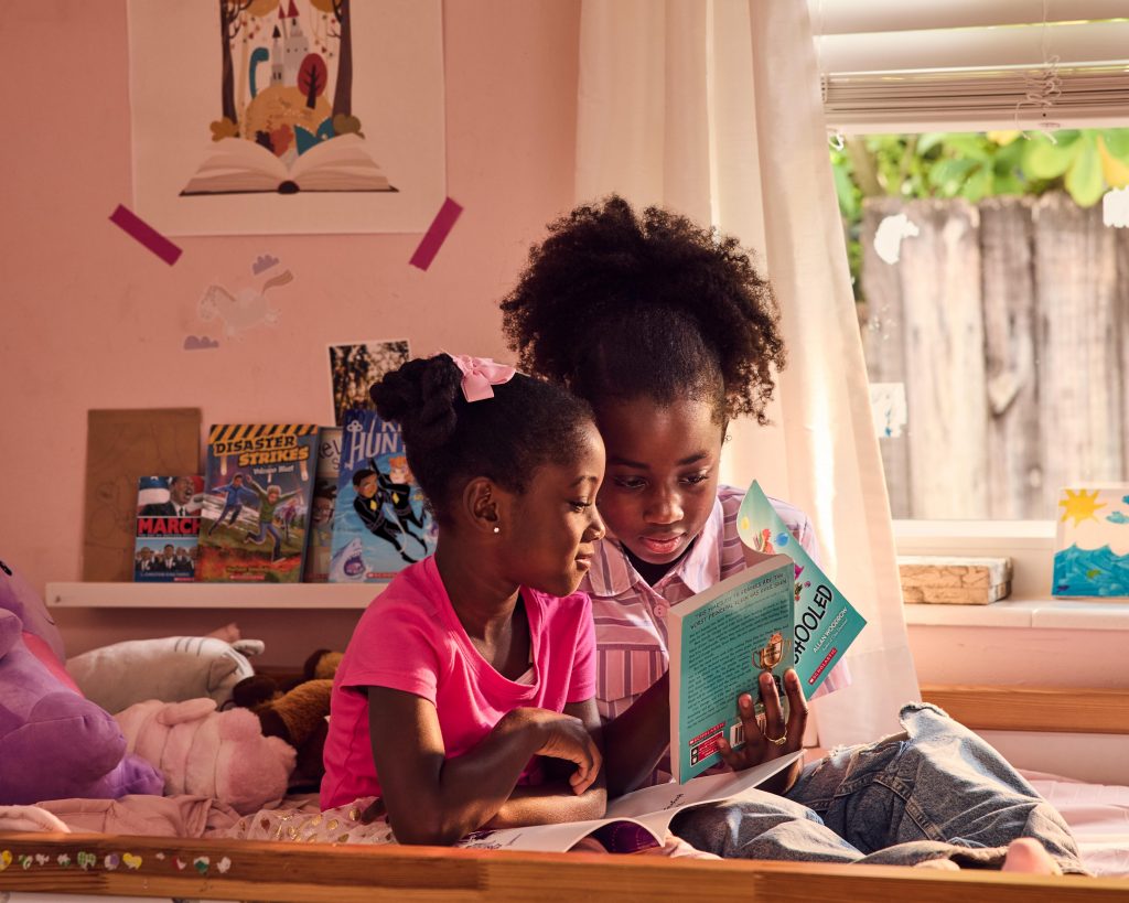 Two sisters read a children's novel on their bed.