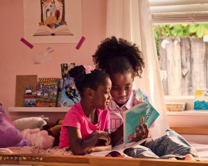 NWRI Two Girls Reading Two sisters read a children's novel on their bed.